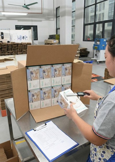 AQL inspection of finished printed packaging boxes, technician measuring product samples for quality and dimensional accuracy.